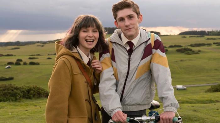Dating Amber movie: Amber laughs next to a smiling Eddie who's perched on a bike, both outdoors in green landscape