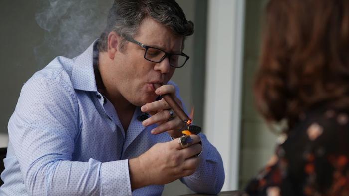 iMordecai Movie: Sean Astin smokes a cigar while sitting across from a woman