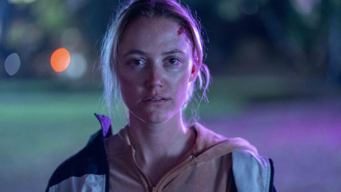 In Cold Light movie: Ava (Maika Monroe), looks at the camera, bloody cuts on her face and wearing two zip up hoodies
