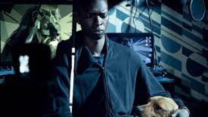 In His Shadow: Black blind man sits at desk with cane and dog by his side