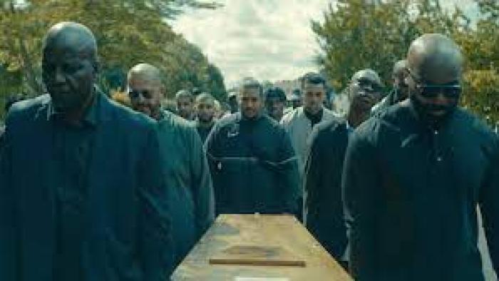 In His Shadow: Pallbearers walk toward camera carrying casket