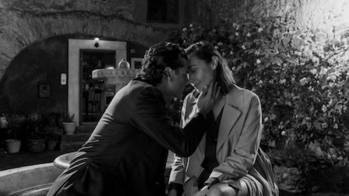 In the Hand of Dante: Couple kisses by a fountain.
