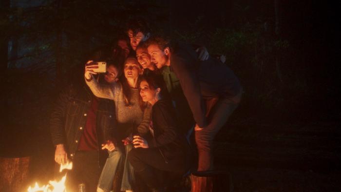 In a Violent Nature Movie: A group of friends assembles for a selfie next to a campfire in the woods at night