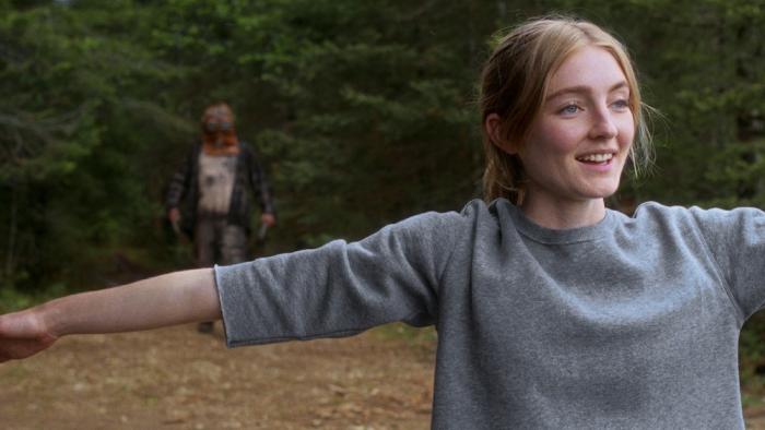 In a Violent Nature Movie: Aurora does yoga stretches in a clearing as the killer creeps up behind her