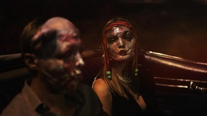 Infinity Pool Movie: Mia Goth wears an eerie mask while looking at Alexander Skarsgard, also in a mask, in the back seat of a convertible
