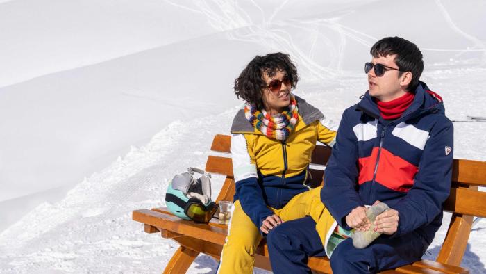 Your Christmas or Mine 2: A young biracial woman and a young White man sit on a bench in the Alps, then man massaging the woman's foot.