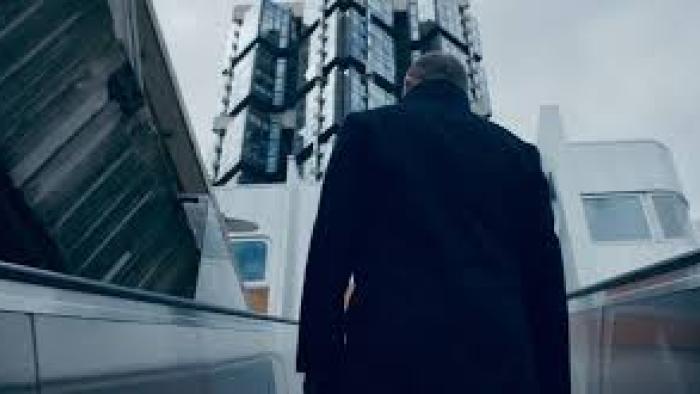 Inside the Trustor Scandal movie: Man in a coat walks up stairs toward a modern building with a cloudy sky above.