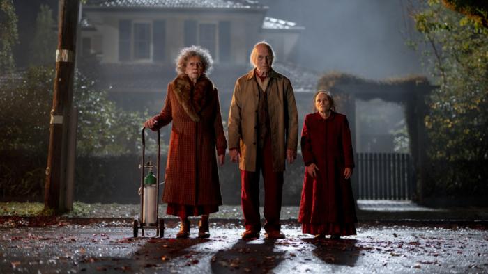 Insidious: Out of the Further Movie: Three unsettling figures wearing red stand in the street, staring