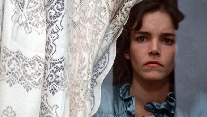 Invasion of the Body Snatchers Movie: Elizabeth (Brooke Adams) peers out a window with a concerned look on her face