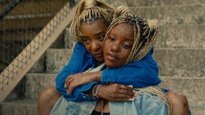 Is God Is movie: Two Black women with braided hair embrace on concrete steps