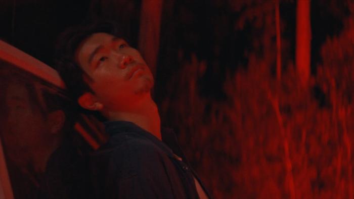 It Ends Movie: Bathed in red light, James (Phinehas Yoon) leans against the car