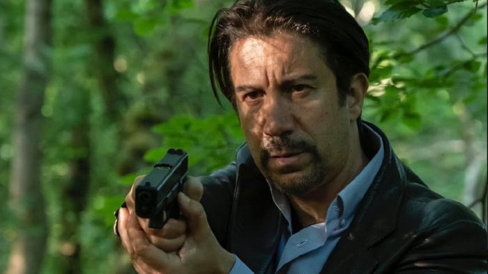 It's Not Over movie: White man with gun holds it in front of him as he walks in wooded area