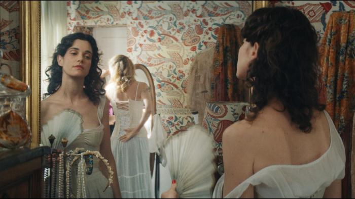 Jane Austen Wrecked My Life movie: Camille Rutherford looks in a mirror wearing 19th century undergarments; a woman is lacing a corset behind her