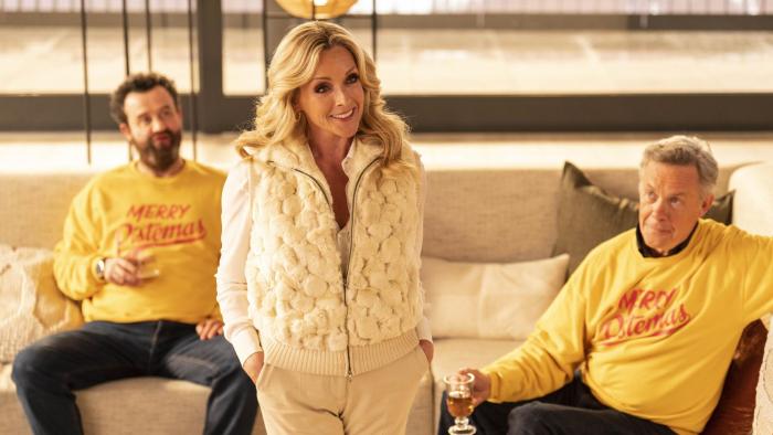 Your Christmas or Mine 2: A White woman dressed all in white smiles as two White men sit down wearing yellow Christmas jumpers and holding drinks.