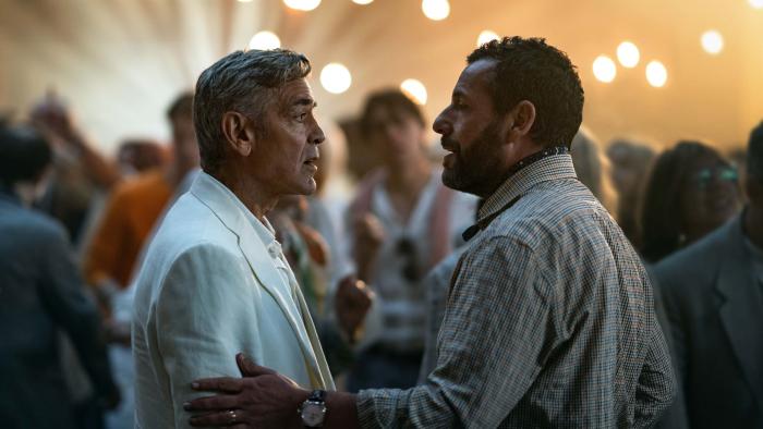 Jay Kelly movie: At a party, Jay (George Clooney) and his manager, Ron (Adam Sandler), have a moment, Ron clutching Jay's arm