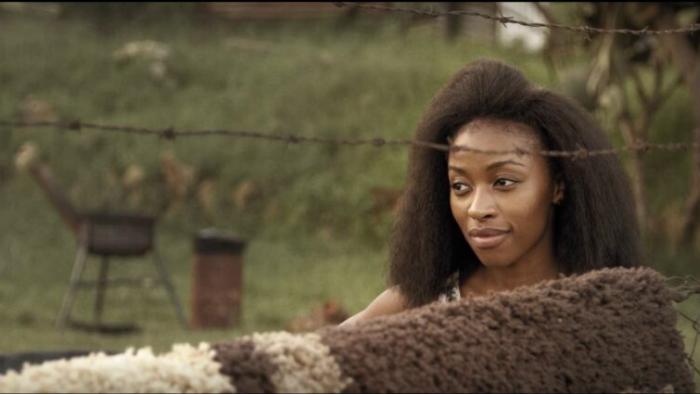 A young woman stands in front of a rural fence.