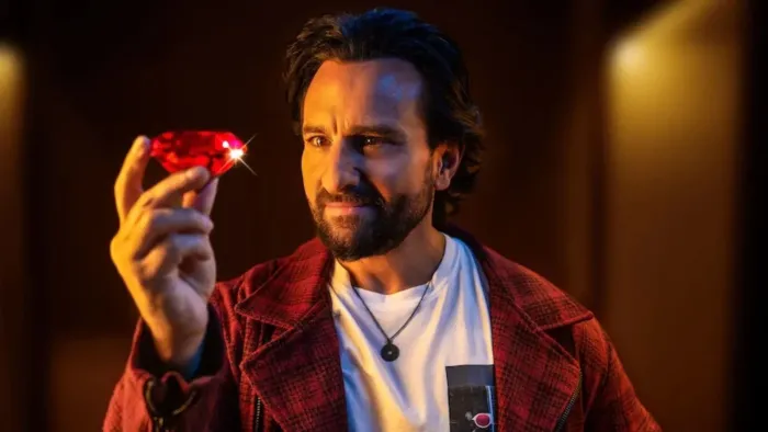 Jewel Thief: The Heist Begins movie: Indian bearded man in white t-shirt and red overcoat center holds up large red diamond
