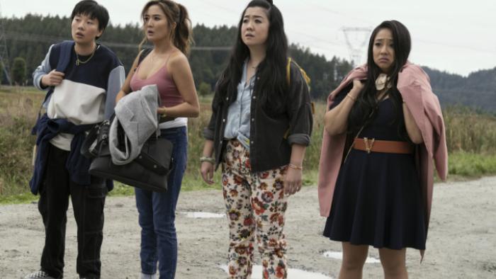 Joy Ride: Four Asian women stand with their arms full of belongings against an empty rural landscape. They all look distressed; one in particular has a downturned mouth and slumped shoulders. 
