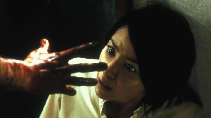 Ju-On—The Grudge: A frightened woman looks at a bloodied hand reaching toward her