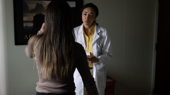 Junction Movie: Mary (Ashley Madekwe), wearing a white lab coat, listens to a patient whose back is to viewers