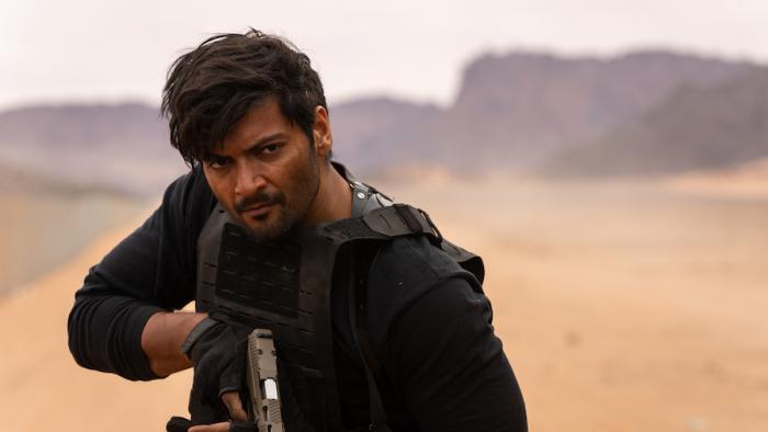 Kandahar Movie: Kahil Nazir, wearing black motorcycle gear and looking determined, raises a pistol
