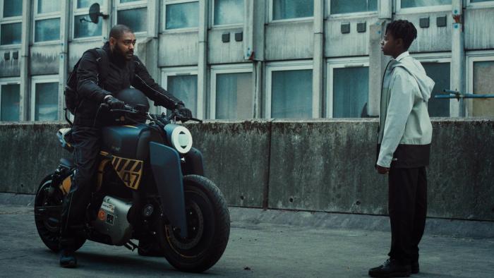 The Kitchen: A Black man rides in on a motorbike toward a young Black teenage boy.