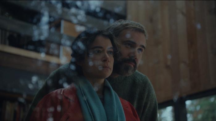 Keeper Movie: Liz and Malcolm look out the window of the cabin, the woods reflecting against the glass