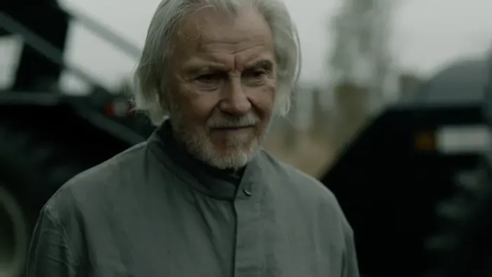 Kill Code: Elderly man with gray hair and beard, standing near a black tractor, dressed in gray