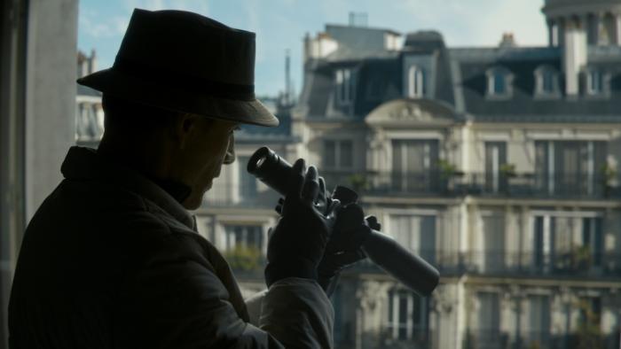 The Killer Movie: Seen from behind, the Killer (Michael Fassbender) checks his rifle scope while looking out the window