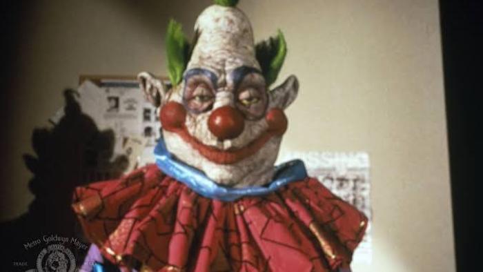 Killer Klowns from Outer Space: Creepy clown with colorful costume and green hair in a dim room.