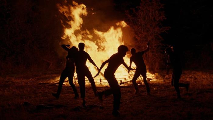 Kindling: Five figures dance around a bonfire in the dark.