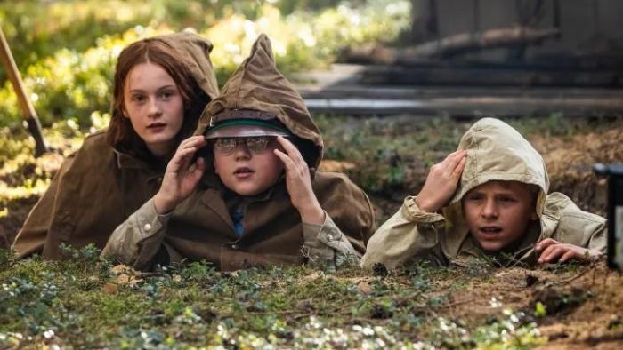 Mr. Car and the Knights Templar movie: Three kids wearing ponchos hunch on the ground as they secretly watch something ahead of them.