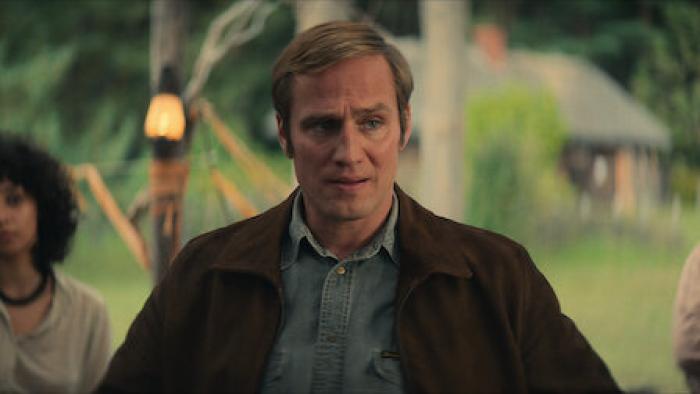 Mr. Car and the Knights Templar movie: A middle aged man in a brown jacket and button down shirt stands with a serious look on his face