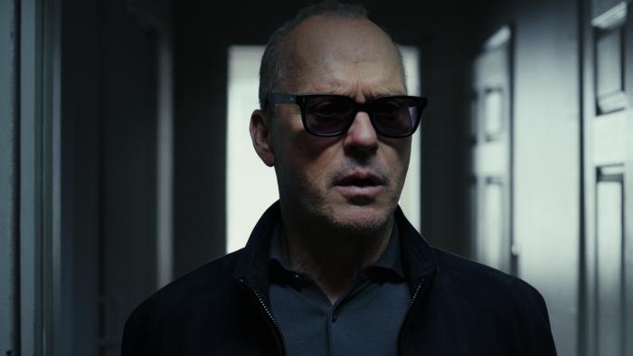 Knox Goes Away Movie: Knox (Michael Keaton) wears dark glasses and a dark coat while standing just inside a doorway
