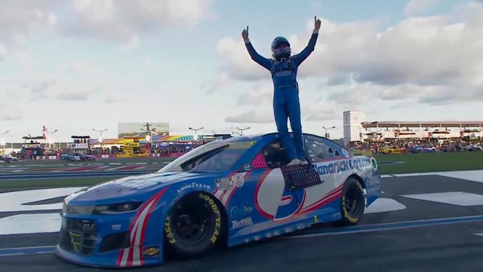 Kyle Larson vs. The Double movie: Kyle Larson in full NASCAR uniform stands on top of his stock car after a win