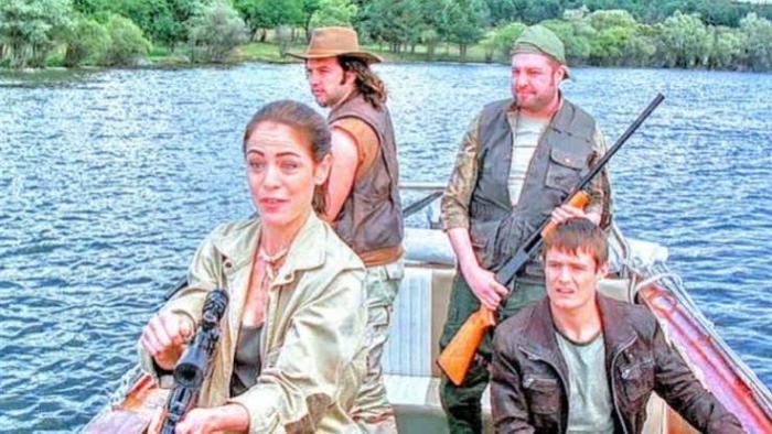 Lake Placid 3: Four people on a boat with rifles, on a lake surrounded by trees.