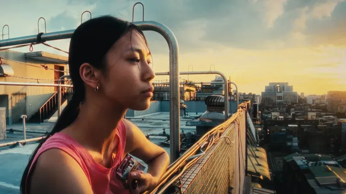 Left-Handed Girl movie: Taiwanese woman with long black hair in braid in red shirt, left, stands on rooftop of apartment building, looking out at city