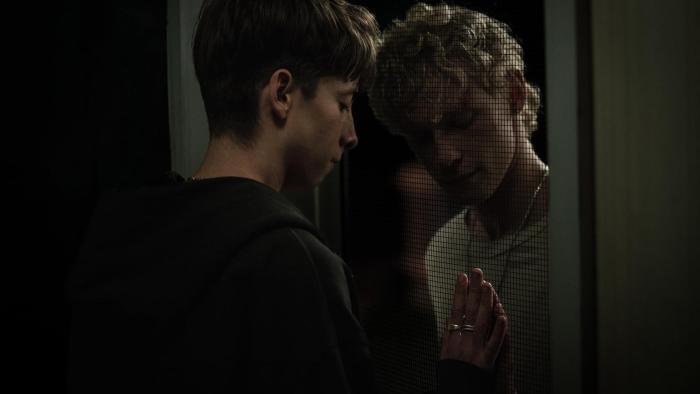Leviticus Movie: Naim and Ryan lovingly touch each other's hands through a screen door