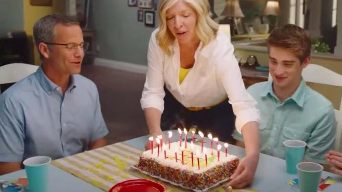 A family of three gather around a birthday cake with lighted candles.