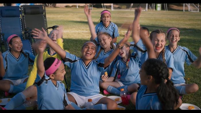 Little Angels movie: A team of 12-year-old girl soccer players cheers while sitting on the ground