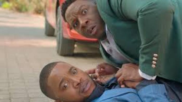 Lobola Man: Black man on ground with other Black man crouched over him 