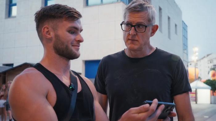 Louis Theroux — Inside the Manosphere: Louis Theroux stands outdoors with a muscular young man in a black tank top who is holding a smartphone