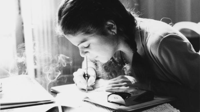 Love, Gilda Movie: Gilda Radner writes at a desk at this close-up picture; a cigarette smoldering on the desk emits smoke. 
