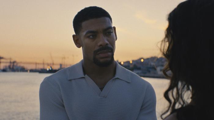Love of Your Life movie: Aaron Pierre is intent as Margaret Qualley tells him something, the bay behind him