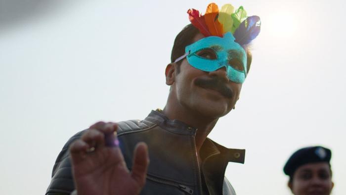 Badhaai Do: An India man wearing a multi-colored face mask smiles and waves. 