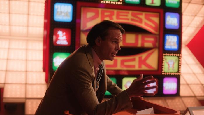 The Luckiest Man in America Movie: Host Peter Tomarken (Walton Goggins) leans forward, as if explaining something