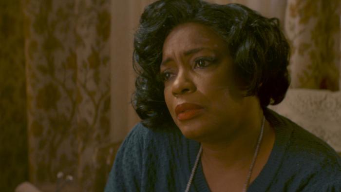 Lucky Strike Movie: Seated, with curtains in the background, Mrs. Caldwell (Aunjanue Ellis-Taylor) looks sad