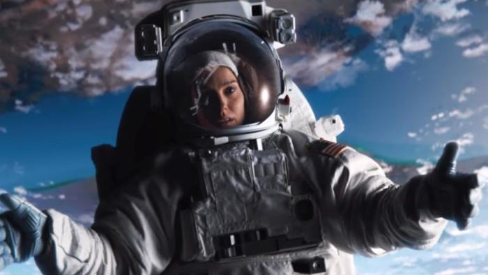Lucy in the Sky Movie: Lucy is silhouetted against a cloudy blue sky while wearing her astronaut suit