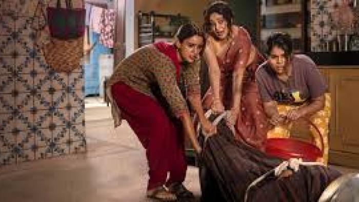 Maa Behen:  Three people in a room, moving a large object wrapped in cloth.
