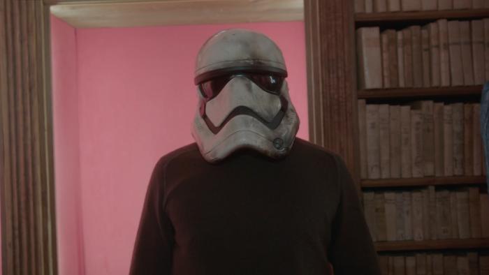 Mad Props Movie: Tom Biolchini stands in front of a bookshelf, trying on a stormtrooper helmet